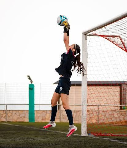 Portera saltando para atrapar el balón bajo palos